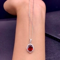 Elegant silver necklace with red oval gemstone and diamond halo pendant worn on hand - Oval Red Diamond Necklace Tz-8