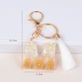 Detail shot of letter M resin keychain with gold leaf, white shell, and tassel measuring 10.5cm - M