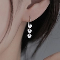Close-up of a silver triple heart drop earring worn on a model with long tassels - Heart Tassel Dangle