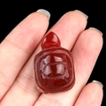 Polished red agate turtle gemstone carving held on a finger against black background - Red Agate