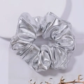 Detail of a shiny silver metallic fabric scrunchie styled with dried flowers on a white plate - Silver