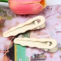 Detail of cream wavy hair clips with a smooth finish on a decorative floral background - Off White