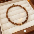 Dettaglio ravvicinato del bracciale di perle di legno marrone scuro con ciondolo dorato - Stile Perla Tonda in Legno di Agar e Disco Dorato / Marrone