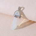 Hexagonal white crystal pendant with silver metal base and loop on beige background - Opalite
