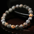 Primo piano del bracciale di perle Yooperlite 8mm con vivace effetto fluorescente arancio - 6mm / Bracciale Minerale UV Fluorescente Arancione Base Grigia (ZJ12674)