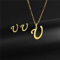 Close-up of golden letter V pendant and matching earrings set on a black pedestal - Letter U / Gold