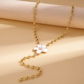 Dettaglio catena dorata a sfere con ciondolo a fiore in smalto bianco su fondo beige - Bianco