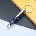 Detailed view of silver metal shock absorber keychain with blue spring on wood - Shock Absorber / Blue