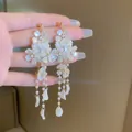 Gros plan détaillé de boucles d'oreilles à pompon avec pétales de perles et strass - Gland de fleur de perle dorée (20#)