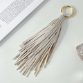 Porte-clés à franges en cuir beige avec anneau doré poli posé sur un livre - Blanc Cassé
