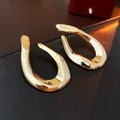 Detailed close-up of glossy gold irregular oval hoop earrings on a leather texture - Gold