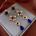 Detail view of vintage golden floral earrings with blue drop gemstones on red silk - Gold Flower Dark Blue Stone Style (11#)