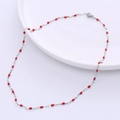 Detail of silver titanium steel necklace with small red enamel lip charms on white plate - Steel + Red Enamel