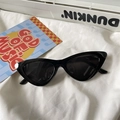 Detail einer glänzenden schwarzen Katzenaugen-Sonnenbrille mit dunklen Gläsern auf Stoff - Cat-Eye / Schwarzer Rahmen Graue Gläser