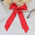 Flat lay of a red satin bow hair tie on a white plush rug with elegant cream roses - Red