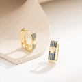 Goldene Huggie-Ohrringe mit blauen Steinen und 3D-Herz auf steinernem Hintergrund - Blauer Strass
