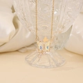 Detail of gold butterfly pendant with iridescent crystals against a white silk background - White