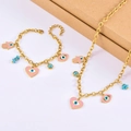 Detailed view of pink heart evil eye and hamsa hand pendants on golden jewelry - Necklace + Bracelet