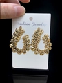 Macro shot of large golden leaf-shaped earrings with metallic texture on display card - Gold Leaf Shape Earrings