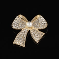 Détail d'une broche nœud dorée ornée de strass et d'une perle sur un fond noir uni - Style B217