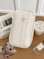 Close-up of quilted cream storage bag with textile label on a wooden desk setting - White