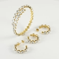 Set di gioielli dorati con bracciale e orecchini tempestati di zirconi su sfondo bianco - Zirconia Bianca