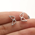 Detailed macro view of hollow angel wing stud earrings held between fingertips - 672 Angel Wings / Steel
