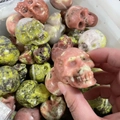 Hand holding a 5cm natural semi-precious stone skull with unique red and brown textures - Pink Tourmaline