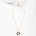 Golden heart pendant necklace with deep red zircon stones on white textured surface - Black Zirconia