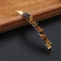 Detailed close-up of a golden hair clip featuring raw tiger eye crystal stones on a dark wood background - Tiger's Eye