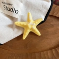 Detailed close-up of a yellow starfish hair clip with realistic textures on a wooden tray - Duckbill Hair Clips / Yellow