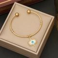Gold evil eye bracelet with radiant sunburst pendant on minimalist jewelry display - White
