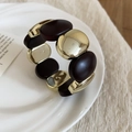 Dettaglio del bracciale elastico vintage in acrilico con metallo dorato e maglie marroni - Stile Ovale / Marrone
