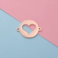 Conector redondo de oro rosa pulido con corazón hueco sobre fondo dividido rosa y azul pastel - Oro rosa