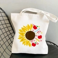 White canvas tote bag featuring sunflower and school stationery print on a black chair - Sunflower Apple Combo