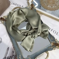 Close-up of a sage green pure silk scarf tied in a bow on a vintage gold tray - 15x150cm / Matcha Green