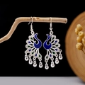 Detail of silver peacock earrings with blue and green enamel hanging on a branch - Blue-Green Enamel Peacock