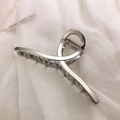 Detailed view of a silver twisted metal hair claw clip on soft white fabric background - Silver-Cross