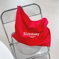 Detail der roten Segeltuchtasche mit weißem SUNDAY-Aufdruck auf modernem Stuhl - Rot