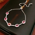 Detaillierte Makroansicht von fünf ovalen roten Zirkonia mit Halo-Fassung auf Silberarmband - Silber-Rosa