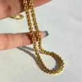 Main tenant un collier en acier inoxydable plaqué or 18k avec maille étoilée sur fond blanc - Collier Or