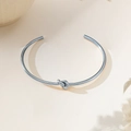 Minimalist silver knot bangle in stainless steel with open-cuff design on beige background - Knot Style (XKB0223) / Steel