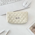 Macro view of beige quilted makeup bag with puppy label on a minimalist white desk - Beige