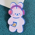 Pink acrylic bunny badge with red headphones and cookie bag on dark green background - Music-Listening Rabbit