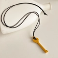 Detailed close-up of golden key pendant with black leather cord on minimalist background - Gold