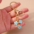 Llavero de flor de cerezo dorado con colgantes de esmalte azul sostenido en la mano - Azul