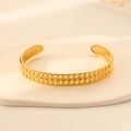 Detail of gold double chain bangle with sun coin pendant on beige wavy surface - Gold Double Chain