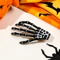 Close-up of black skeleton hand hair clip with white bone details on festive background - Black
