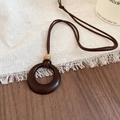 Detail view of round resin pendant with bead on a brown cord over a wooden table - Brown Round Ring Style