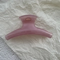 Detailed view of a pink translucent curved hair claw clip on a minimalist textured surface - Pink